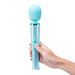 Hand holding a glittery blue Le Wand Petite massager with rounded head and two-button control on white background.