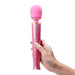 Hand holding a pink glittery Le Wand Petite massager with a rounded head and two control buttons.