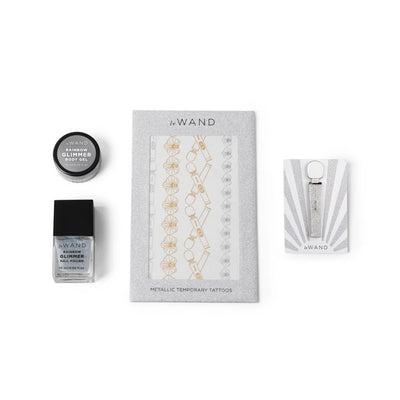Le Wand All That Glimmers set accessories including rainbow glimmer body gel, nail polish, metallic temporary tattoos, and enamel pin on white background.