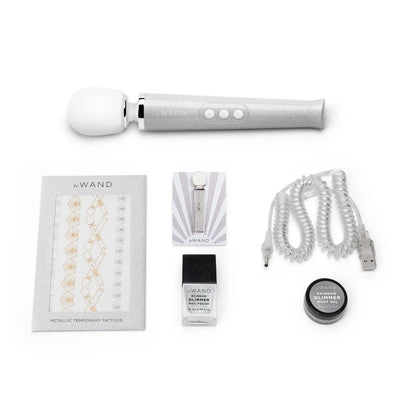 Le Wand Petite vibrator with metallic temporary tattoos, glittery enamel pin, rainbow glimmer nail polish, body gel, and coiled USB charging cable.
