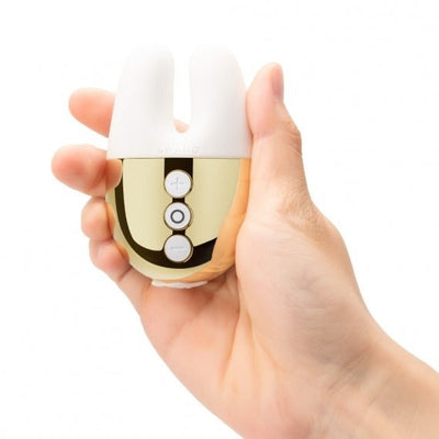 Hand holding compact Le Wand Double Vibe with white silicone bunny ears and gold control panel with buttons.