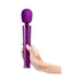 Hand holding a purple Le Wand Petite rechargeable massager with control buttons visible on the handle.