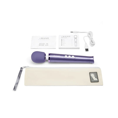 Purple Le Wand Petite rechargeable massager with USB charging cable, user guides, and beige travel pouch on white background.