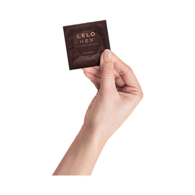 Hand holding a single LELO HEX Respect XL condom in dark brown packaging against a white background.