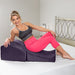 Woman reclining on a plum-colored Liberator Flip Ramp pillow on a bed, demonstrating its ergonomic support and comfort.