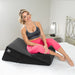Woman in athletic wear sitting comfortably on a black Liberator Wedge/Ramp Combo cushion on a bed.