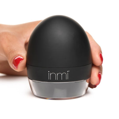 Hand holding black dome-shaped inmi personal care device with clear base on white background