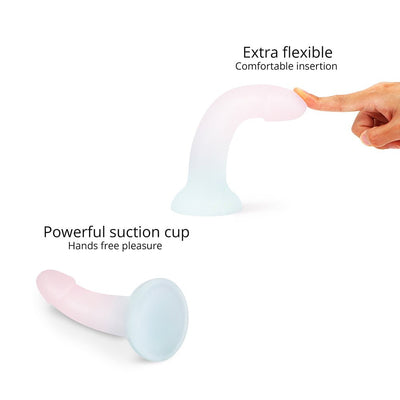 Flexible pastel-colored dildo with glitter and suction cup base shown bending under a fingertip for comfortable insertion.