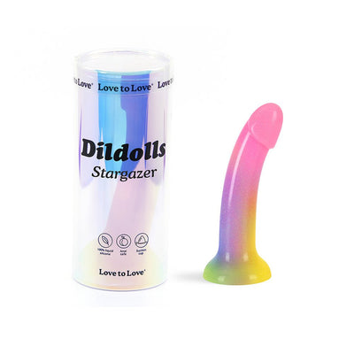 Curved rainbow-colored dildo with glitter and suction cup next to iridescent cylindrical packaging labeled Dildolls Stargazer.
