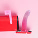 Pink and purple gradient silicone dildo with multicolor star glitter standing inside a red mailbox against a pink background.