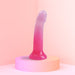 Pink and purple gradient silicone dildo with multicolor star glitter and suction base on a pastel pink pedestal.