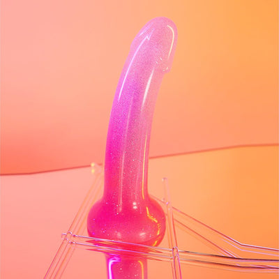 Pink and purple gradient silicone dildo with multicolor star glitter and suction base on reflective surface.