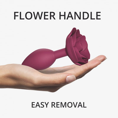 Hand holding a medium plum silicone anal plug with a rose-shaped handle for easy removal.
