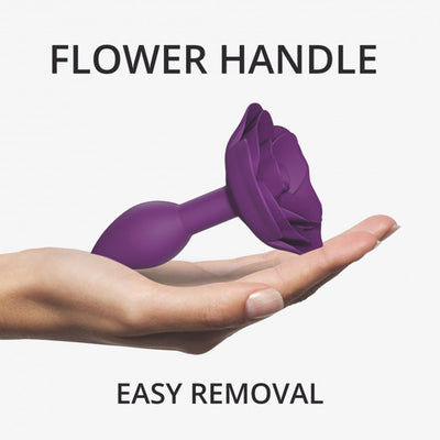 Hand holding a small purple silicone anal plug with a rose-shaped handle for easy removal.
