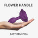 Hand holding a small purple silicone anal plug with a rose-shaped handle for easy removal.