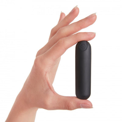 Hand holding a compact black bullet vibrator with a power button on top against a white background.