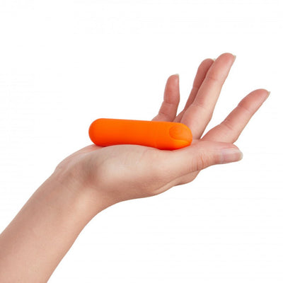 Hand holding a compact, bright orange rechargeable bullet vibrator with a smooth, rounded design.