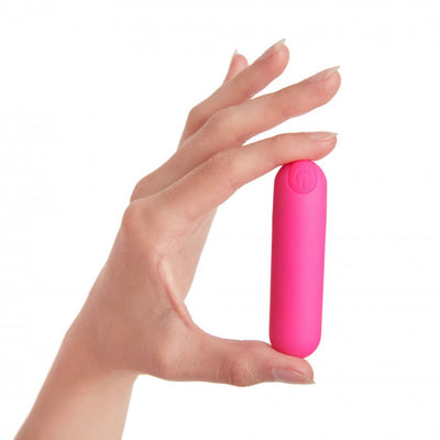 Hand holding compact pink bullet vibrator with power button on top against white background.