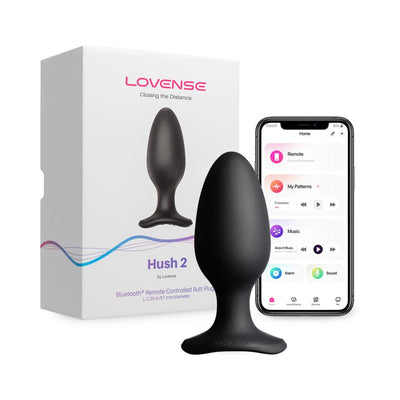 Lovense Hush 2 black silicone butt plug with flared base next to its packaging and smartphone showing app controls.