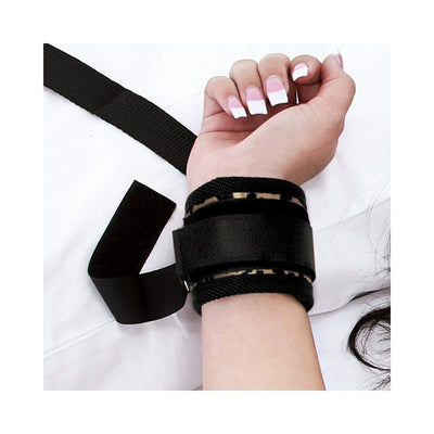 Close-up of a wrist secured in a black adjustable restraint cuff with soft lining on a white surface.