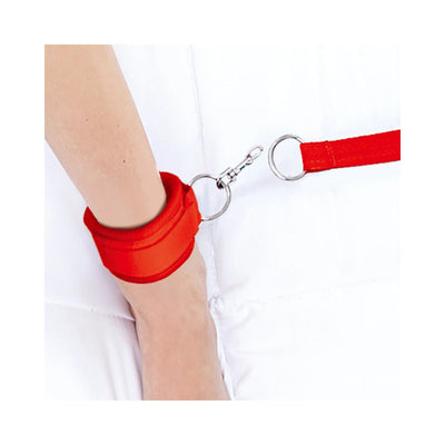 Red adjustable neoprene wrist cuff connected to a metal ring and clip restraint on a white surface.