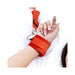 Close-up of a wrist secured in a bright red adjustable restraint cuff attached to a white bedspread system.