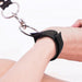 Close-up of a wrist secured with an adjustable black cuff attached to a metal hogtie connector ring.