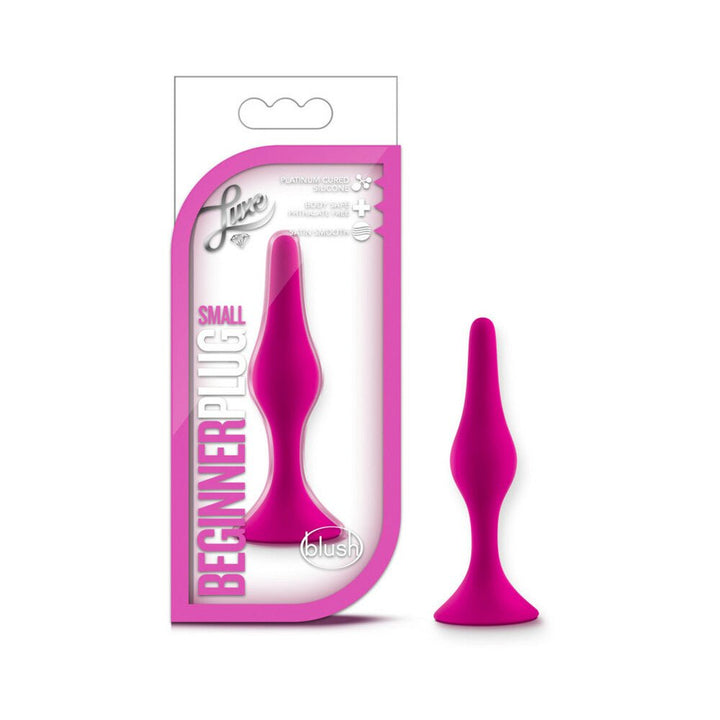 Small magenta beginner butt plug with tapered tip and flared base next to its pink and white packaging.
