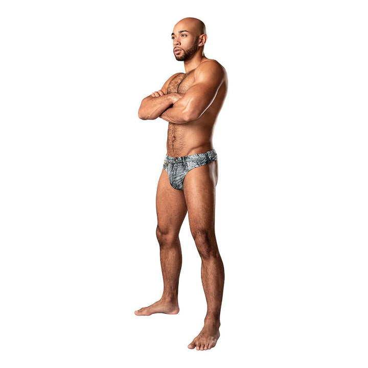 Male model wearing Male Power Dirty Denim Thong with a denim print and contoured pouch, standing with arms crossed.