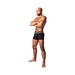 Athletic man wearing black Male Power Infinite Comfort amplifying strappy pouch shorts with dual logo waistbands, standing with arms crossed.