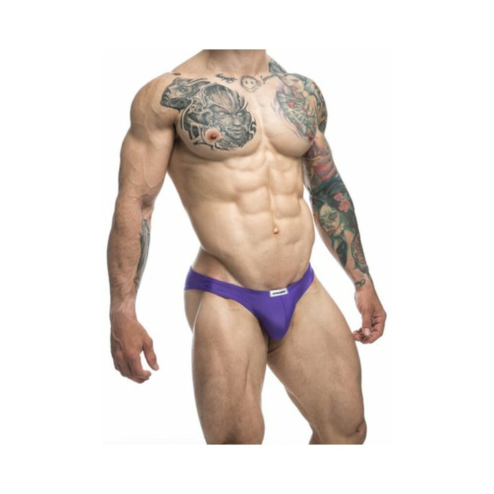 Muscular male model wearing purple Malebasics Justin + Simon classic bikini underwear with tattooed arms and chest.