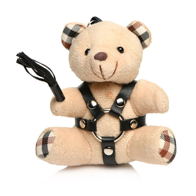 Plush light peach teddy bear keychain wearing black faux leather harness and holding a mini black flogger with plaid ear and paw accents.