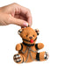 Hand holding a small brown teddy bear keychain with black straps, silver chains, and a red ball gag accessory.