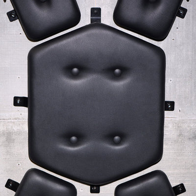 Close-up of black padded PVC faux leather cushions from a wall-mounted St. Andrew's Cross against a concrete background.