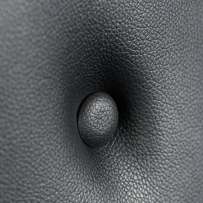 Close-up of black textured PVC faux leather upholstery with a centered button tuft detail.