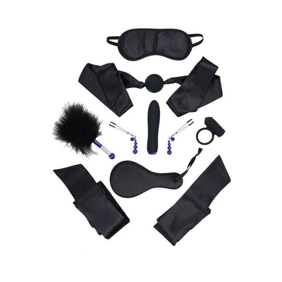 Black satin blindfold, ball gag, wrist restraints, paddle, feather tickler, nipple clamps, vibrator, and cock ring set arranged on white background.