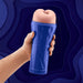 Hand holding a blue ergonomic stroker with a soft, flesh-toned textured sleeve against a dark blue abstract background.