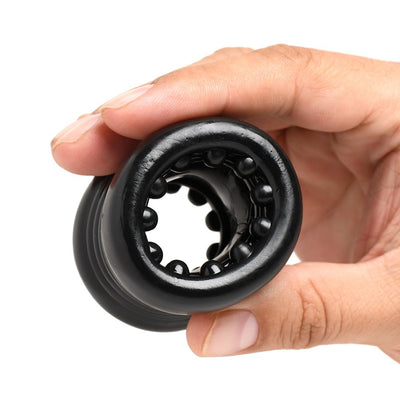 Hand holding a black stacked ball stretcher with textured nubs inside the tunnel made of stretchy TPE material.