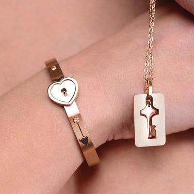 Rose-gold locking bracelet with heart-shaped clasp worn on wrist paired with matching key necklace on chain.