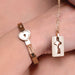Rose-gold locking bracelet with heart-shaped clasp worn on wrist paired with matching key necklace on chain.