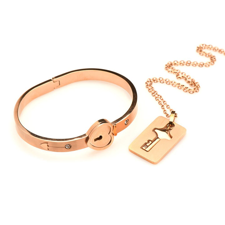 Rose-gold locking bracelet with heart-shaped clasp and matching key necklace on a chain, elegant tungsten steel design.