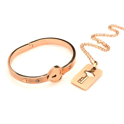 Rose-gold locking bracelet with heart-shaped clasp and matching key necklace on a chain, elegant tungsten steel design.