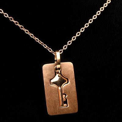 Rose-gold plated tungsten steel key pendant necklace with a cut-out key design on a delicate chain against black background.