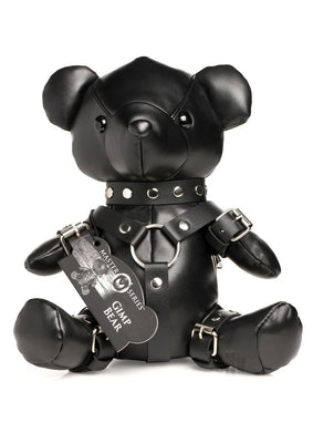Black vegan leather teddy bear dressed in detailed gimp harness and collar with silver hardware, sitting upright.
