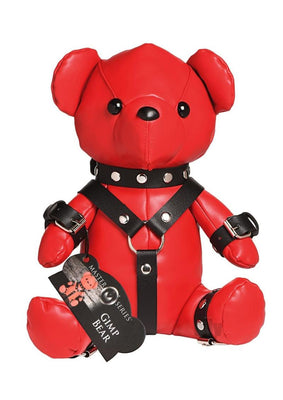 Red vegan leather teddy bear wearing black gimp harness straps and cuffs with silver studs and buckles.