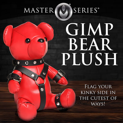Red vegan leather teddy bear wearing black gimp-style straps and collar, sitting on a wooden surface.