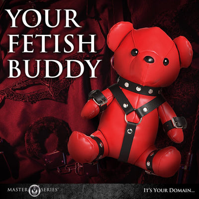Red vegan leather teddy bear dressed in black gimp harness and cuffs, styled as a playful fetish accessory.