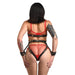 Back view of a woman wearing a black adjustable vegan leather harness with gold accents and matching wrist cuffs over red lingerie.