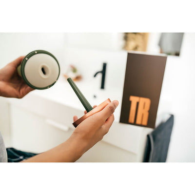 Hands holding the MYHIXEL TR device and its detachable cap with the product box in the background on a bathroom counter.
