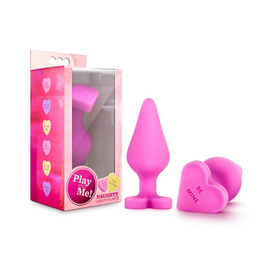 Pink silicone anal plug with heart-shaped base and "Be Mine" text, displayed next to its colorful packaging.